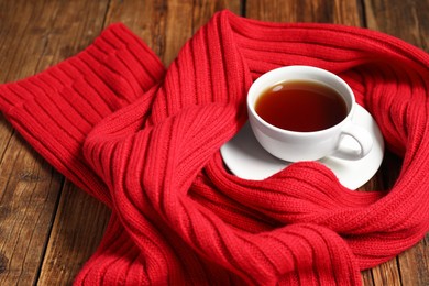 Red knitted scarf and tea on wooden table, closeup