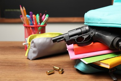 Photo of Gun, bullets and school stationery on wooden table near blackboard indoors, closeup