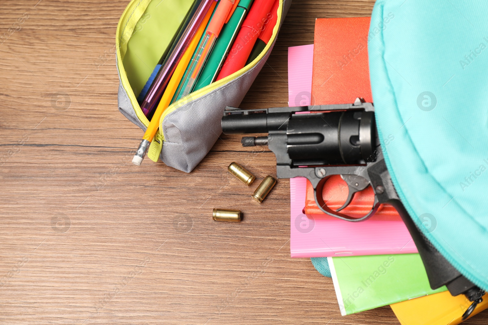 Photo of Gun, bullets and school stationery on wooden table, flat lay. Space for text