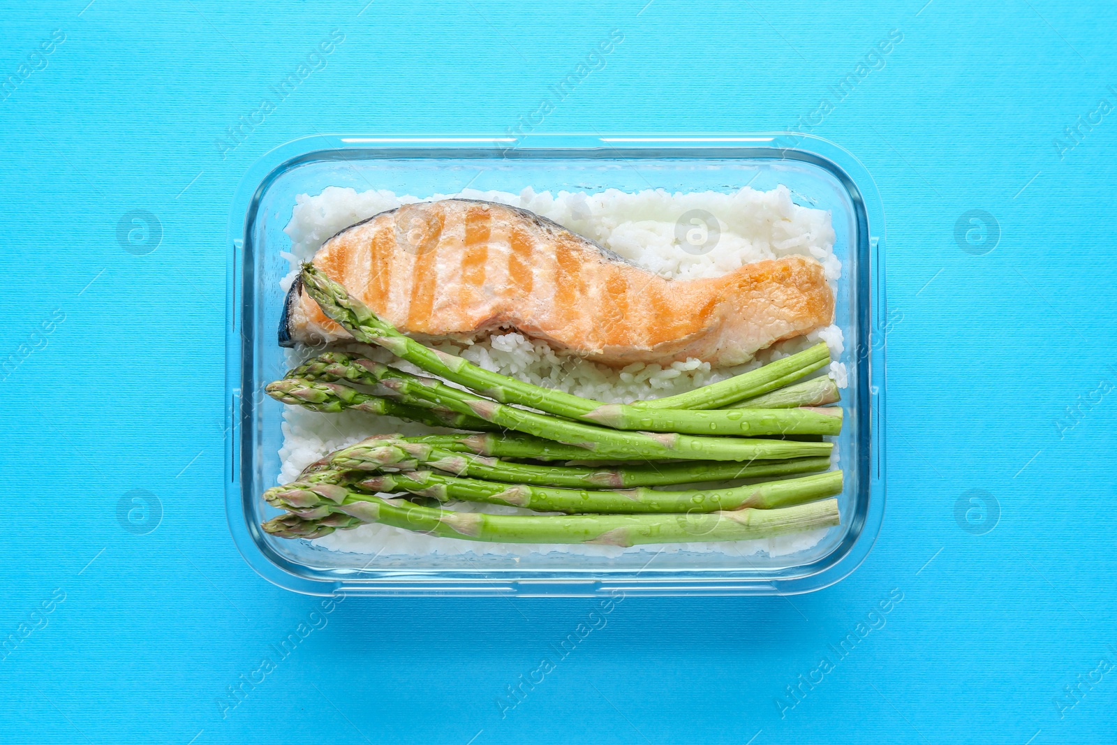 Photo of Healthy meal. Fresh asparagus, salmon and rice in glass container on light blue background, top view