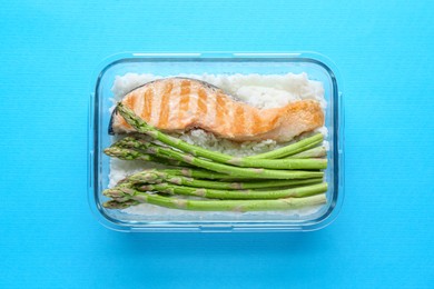 Healthy meal. Fresh asparagus, salmon and rice in glass container on light blue background, top view