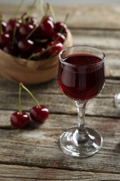 Photo of Delicious cherry liqueur in glass and fresh berries on wooden table