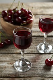 Photo of Delicious cherry liqueur in glasses and fresh berries on wooden table