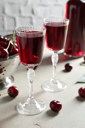 Delicious cherry liqueur in glasses and fresh berries on light grey table