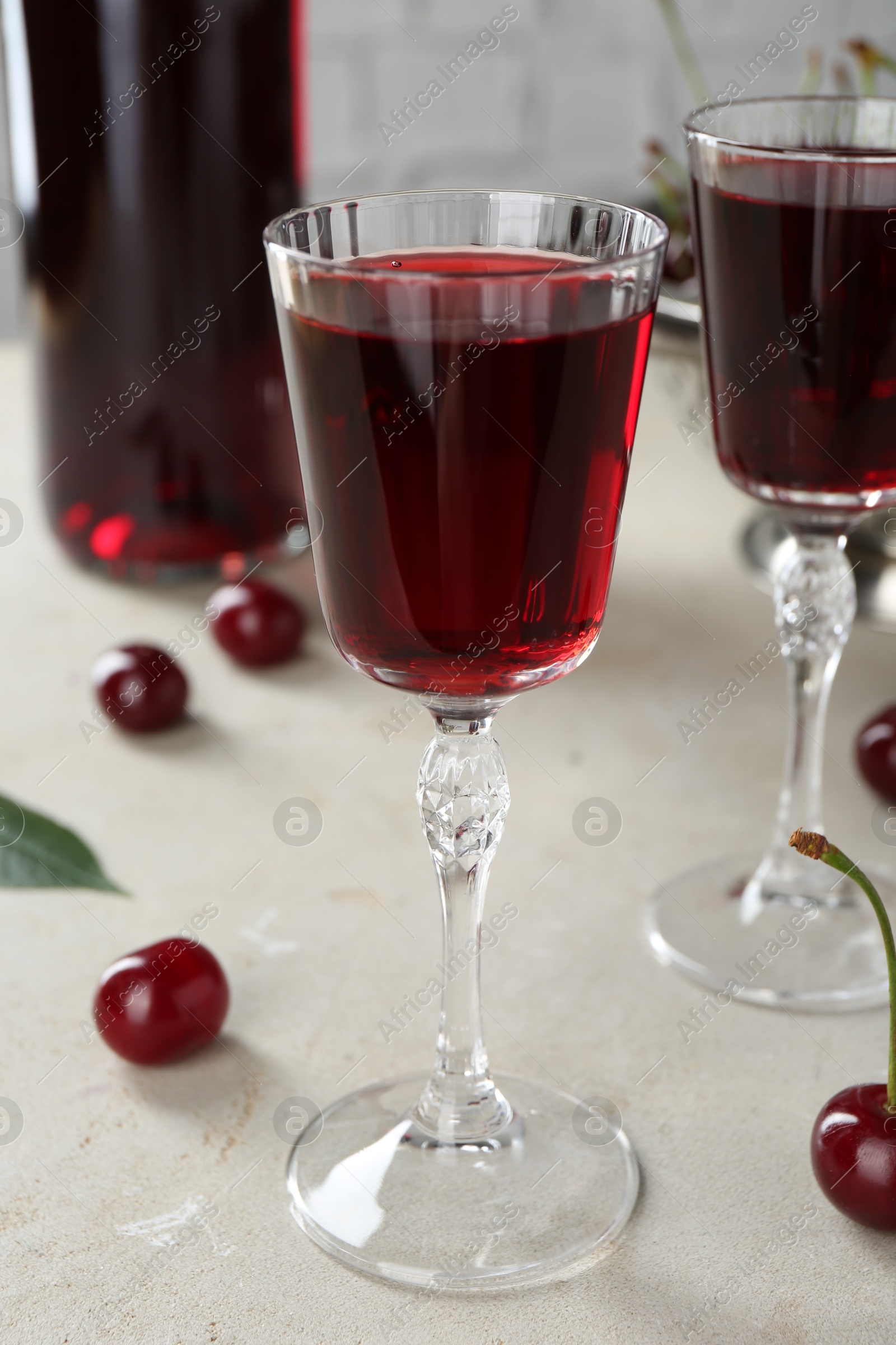 Photo of Delicious cherry liqueur in glasses and fresh berries on light grey table