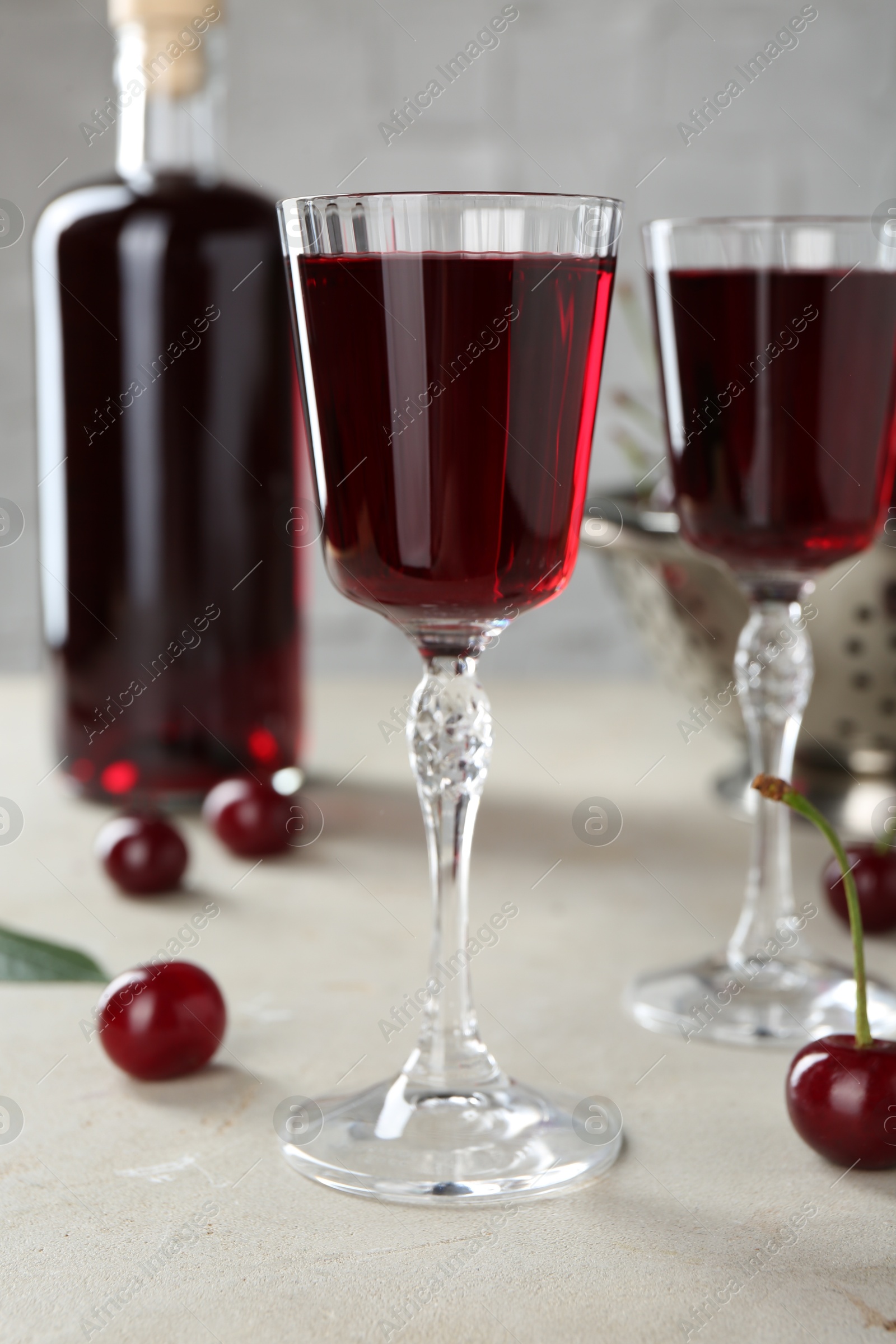 Photo of Delicious cherry liqueur in glasses, fresh berries and bottle on light grey table