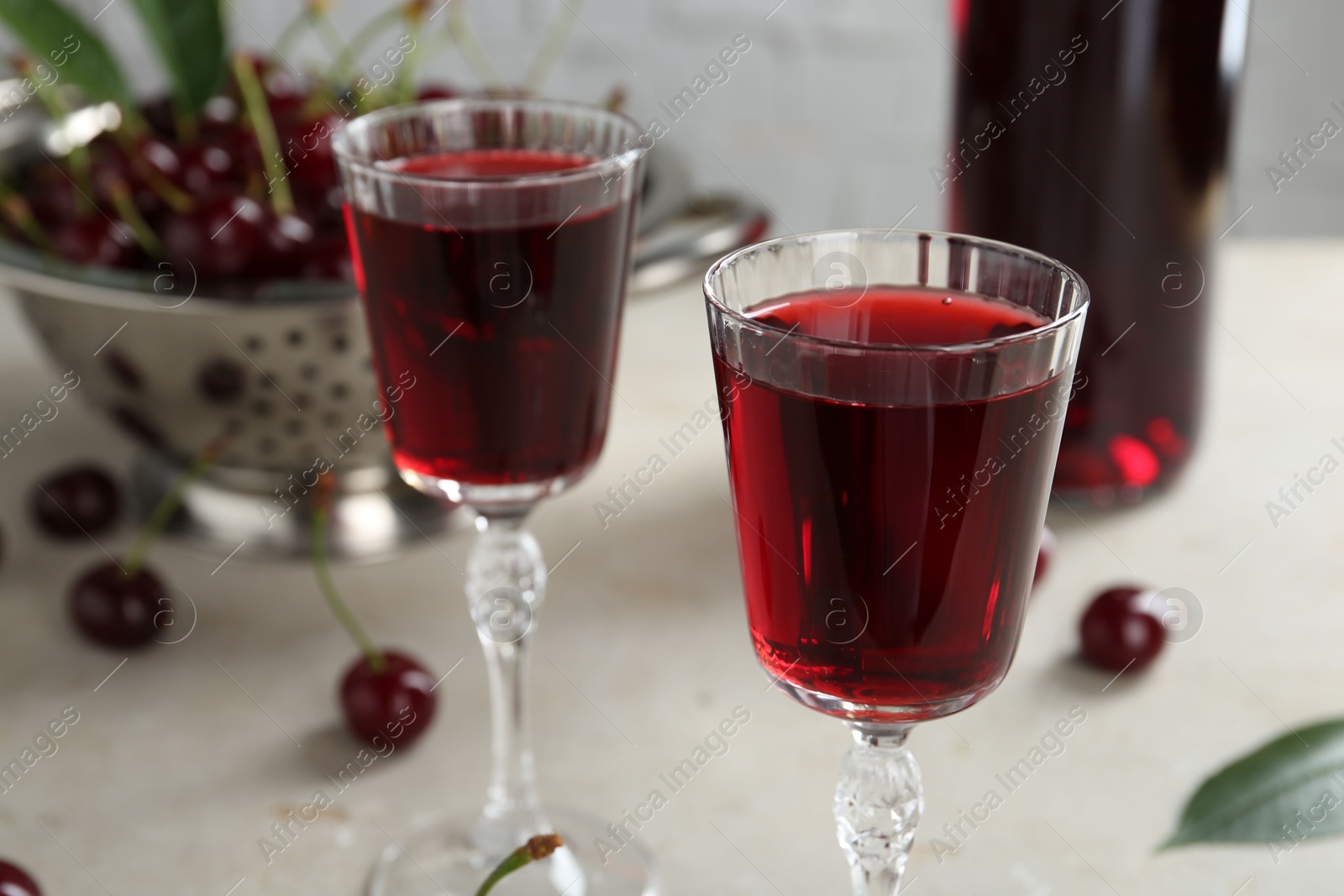 Photo of Delicious cherry liqueur in glasses and fresh berries on light grey table