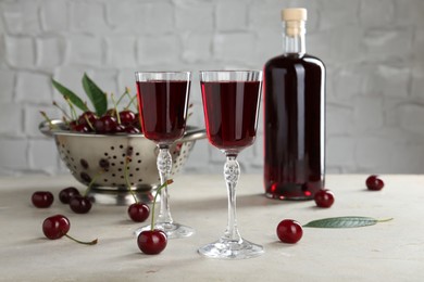 Delicious cherry liqueur in glasses, fresh berries and bottle on light grey table