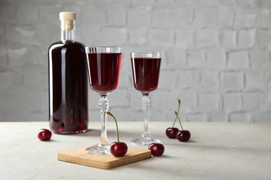 Photo of Delicious cherry liqueur in glasses, bottle and fresh berries on light grey table, space for text