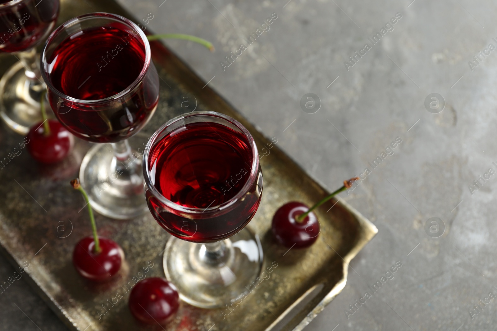 Photo of Delicious cherry liqueur in glasses and fresh berries on grey table, space for text