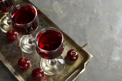 Photo of Delicious cherry liqueur in glasses and fresh berries on grey table, space for text
