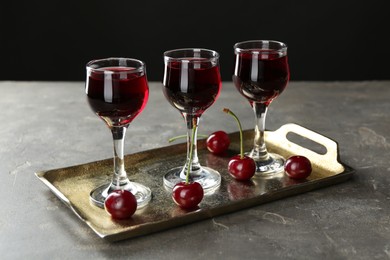 Photo of Delicious cherry liqueur in glasses and fresh berries on grey table