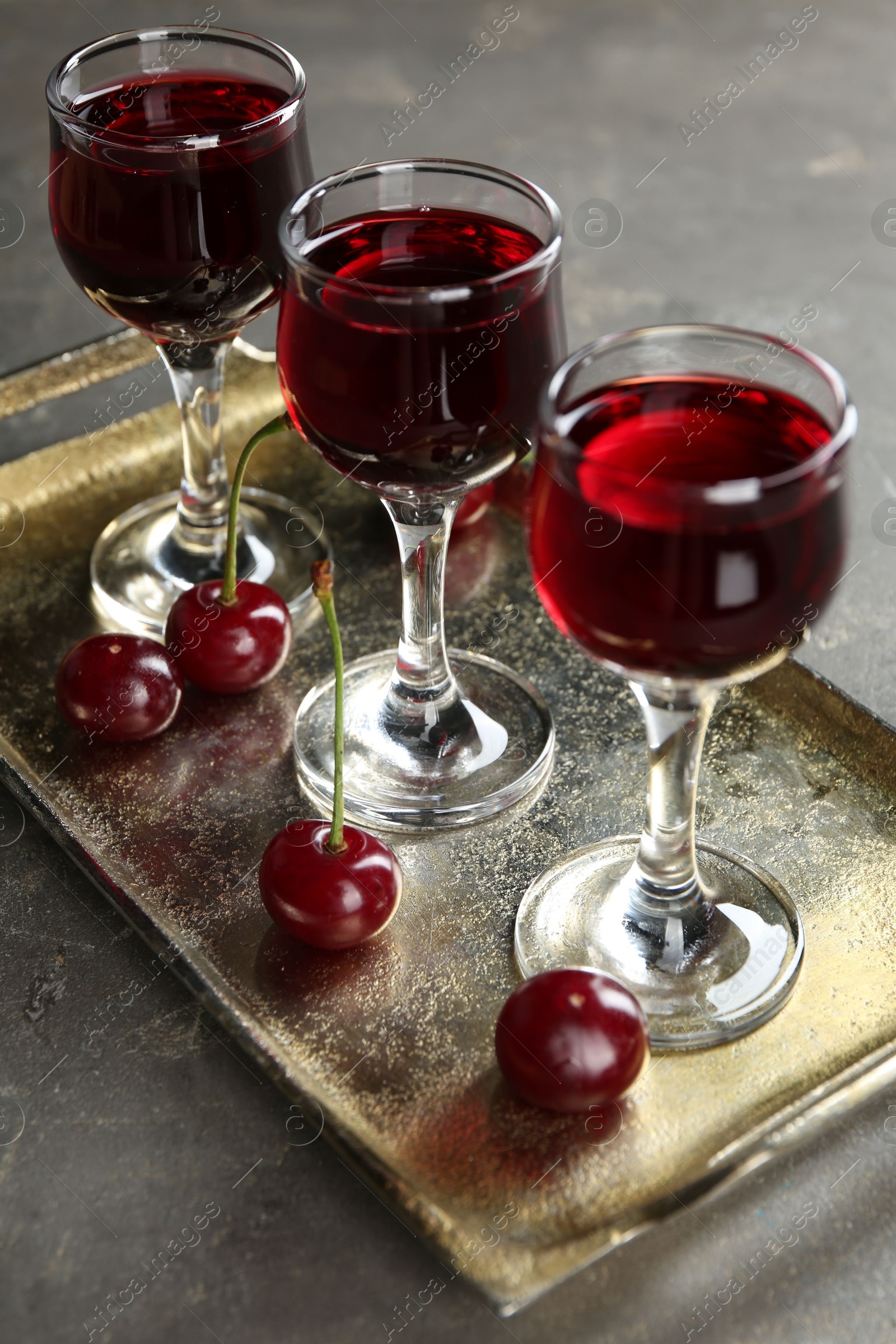 Photo of Delicious cherry liqueur in glasses and fresh berries on grey table