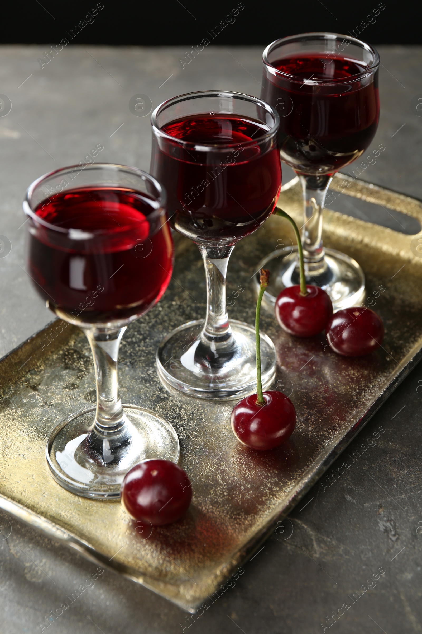 Photo of Delicious cherry liqueur in glasses and fresh berries on grey table