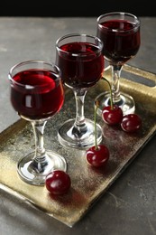 Delicious cherry liqueur in glasses and fresh berries on grey table