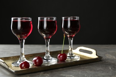 Photo of Delicious cherry liqueur in glasses and fresh berries on grey table