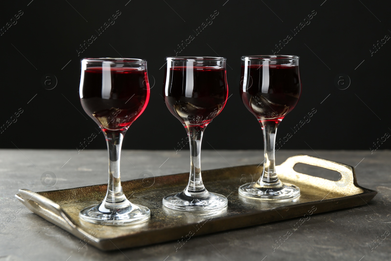 Photo of Delicious cherry liqueur in glasses on grey table