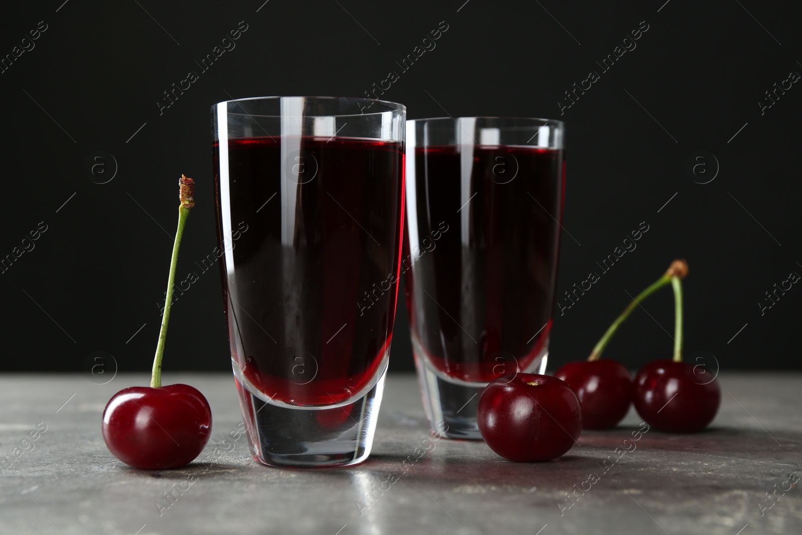 Photo of Delicious cherry liqueur in shot glasses and fresh berries on grey table, closeup