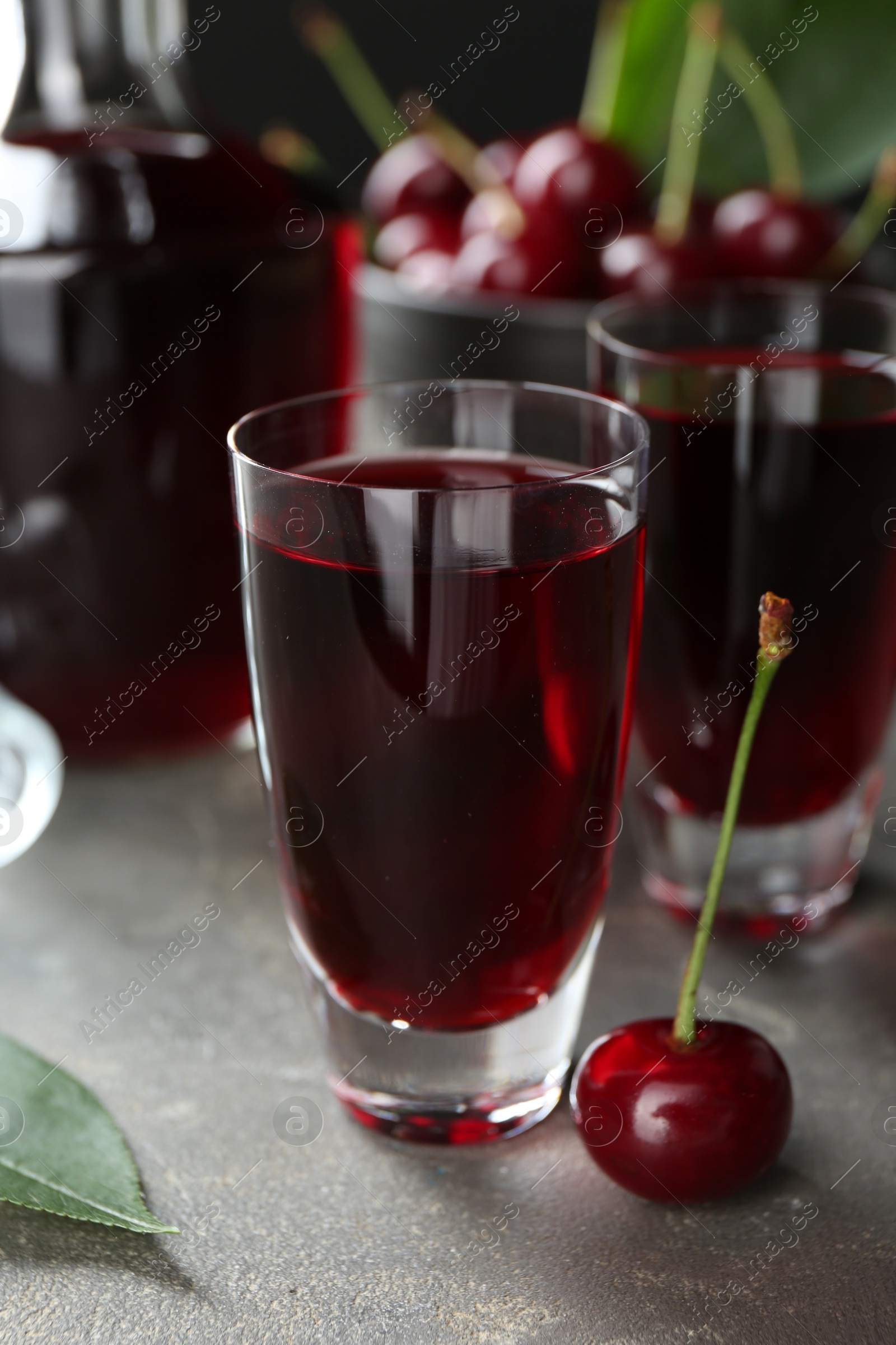 Photo of Delicious cherry liqueur in shot glasses and fresh berries on grey table