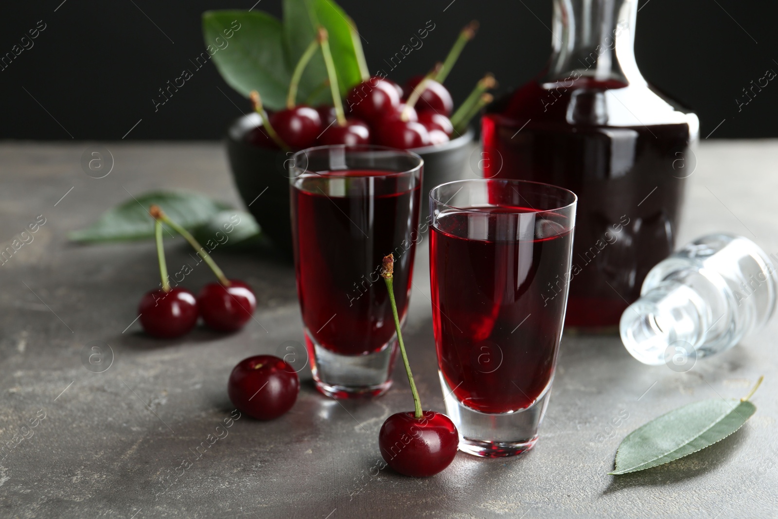 Photo of Delicious cherry liqueur in shot glasses, decanter and fresh berries on grey table