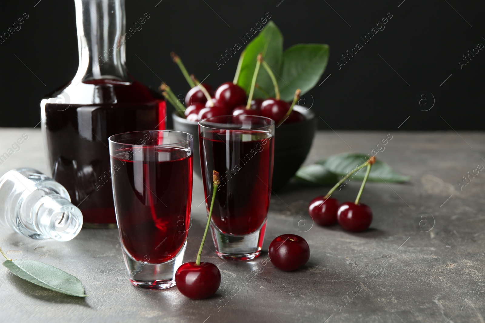 Photo of Delicious cherry liqueur in shot glasses, decanter and fresh berries on grey table