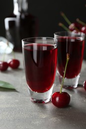 Delicious cherry liqueur in shot glasses and fresh berries on grey table