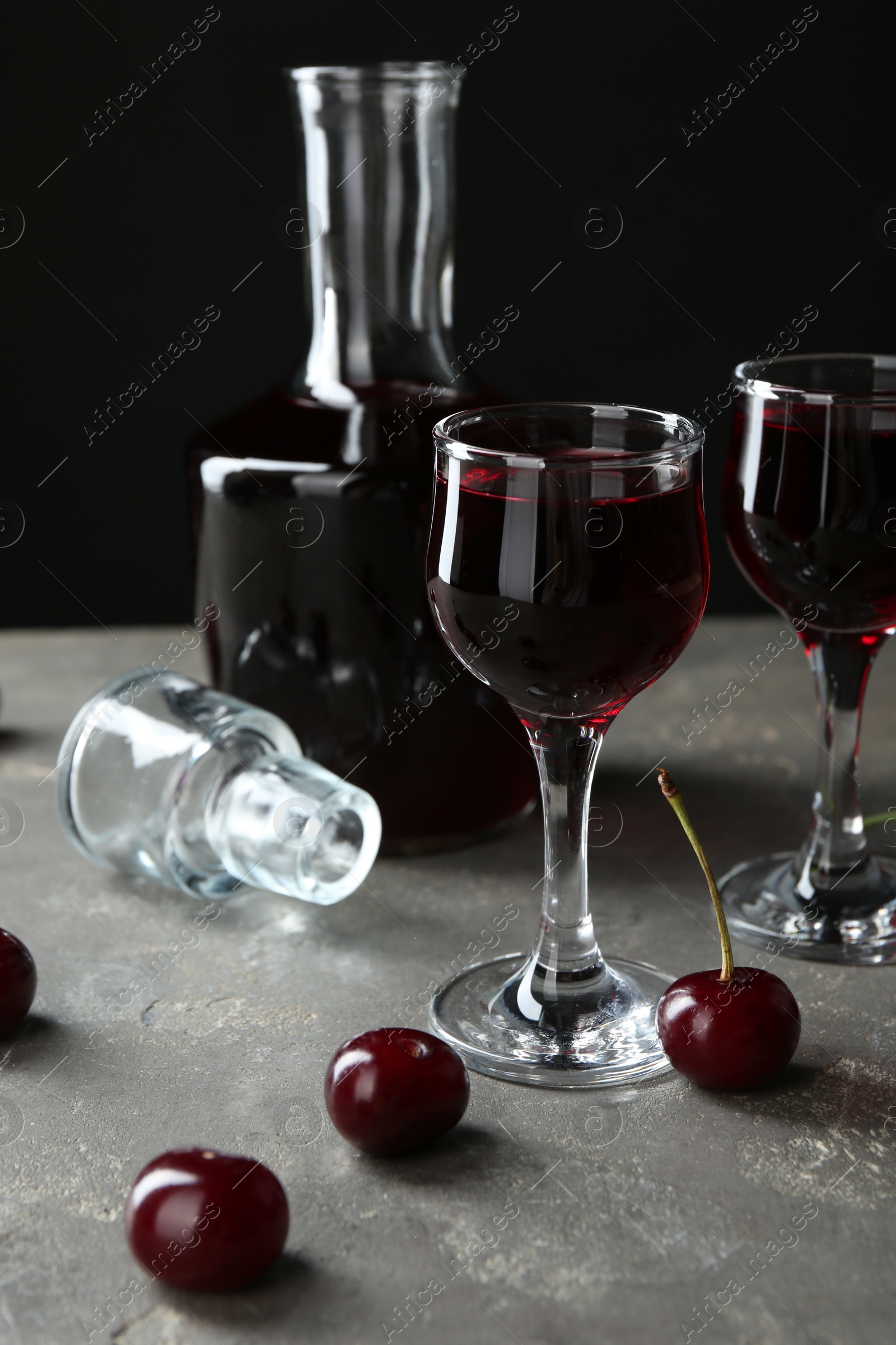 Photo of Delicious cherry liqueur in glasses, decanter and fresh berries on grey table