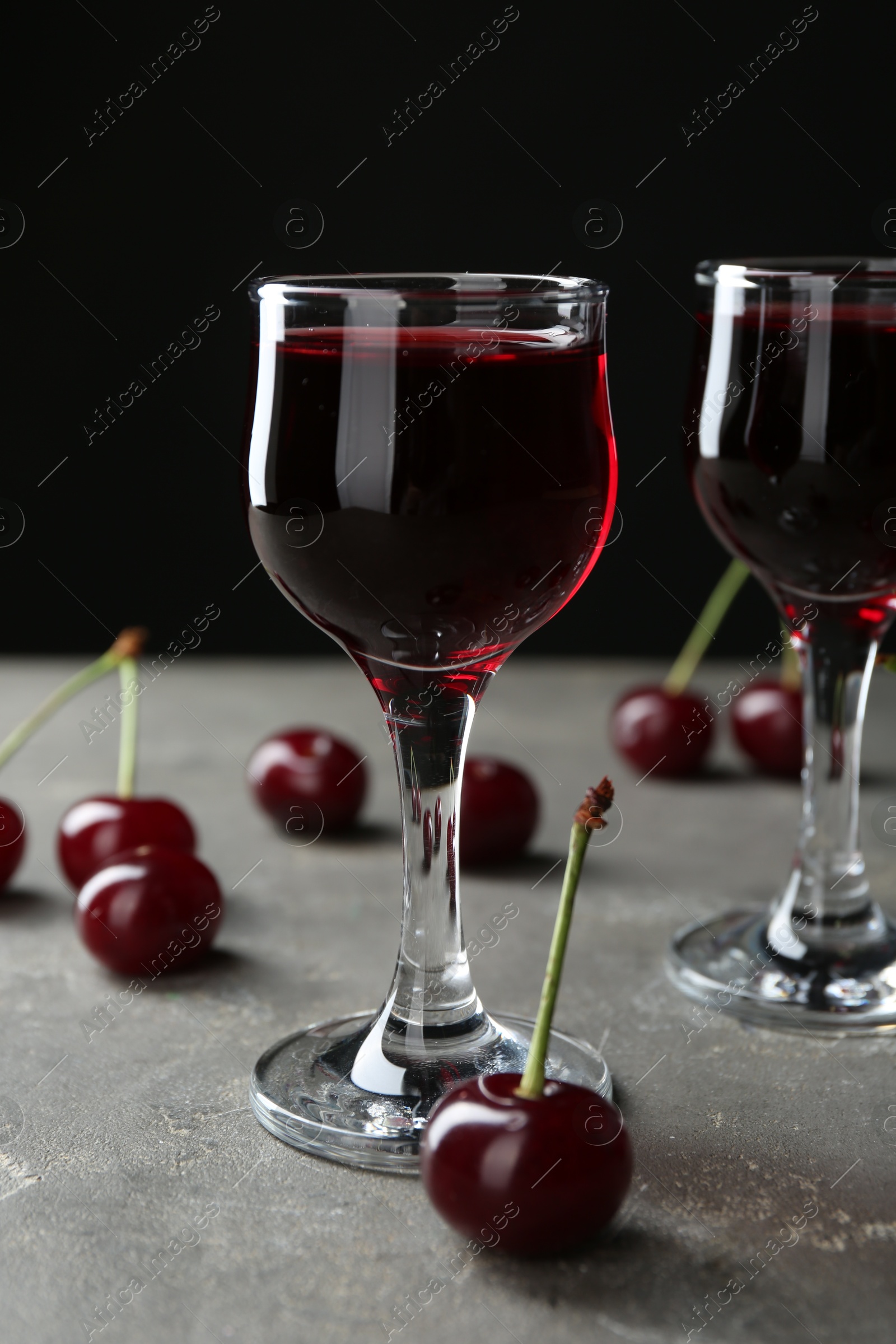 Photo of Delicious cherry liqueur in glasses and fresh berries on grey background