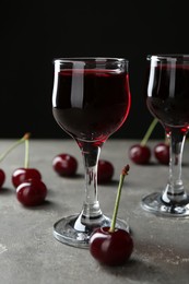 Delicious cherry liqueur in glasses and fresh berries on grey background