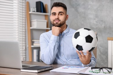 Young man with soccer ball at table in office