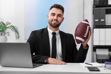 Photo of Young man with american football ball at table in office