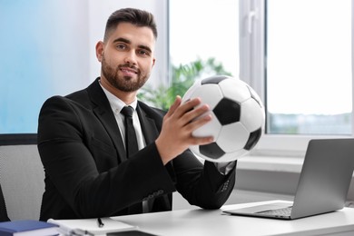 Photo of Young man with soccer ball at table in office