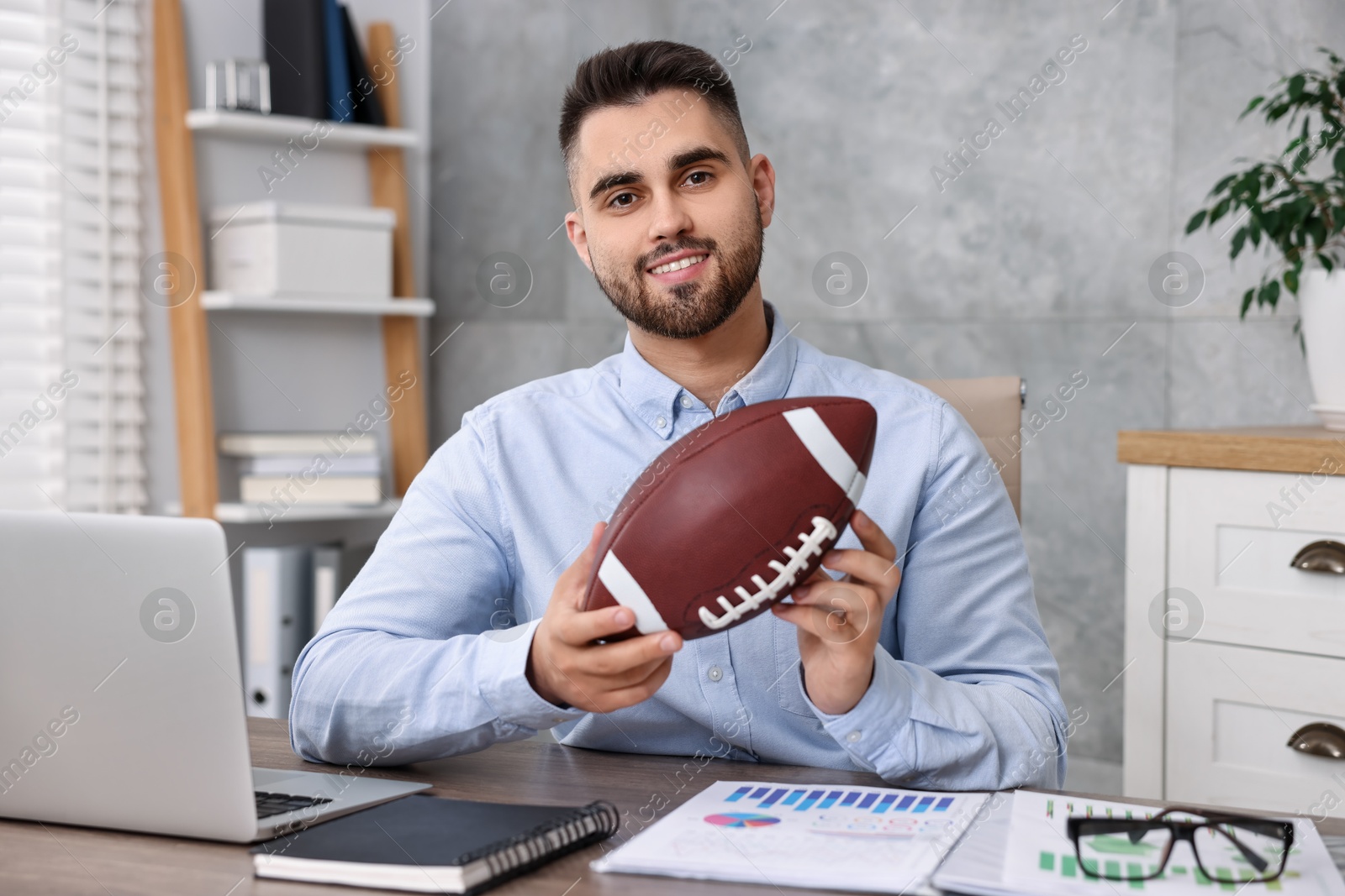 Photo of Young man with american football ball at table in office