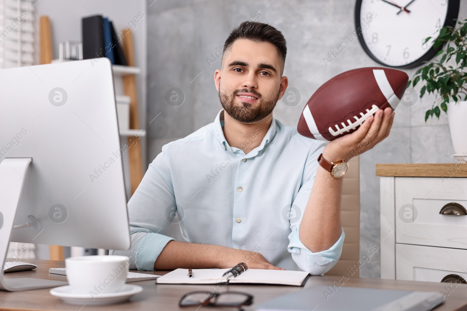 Photo of Young man with american football ball at table in office