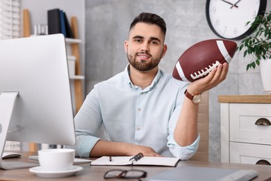 Young man with american football ball at table in office