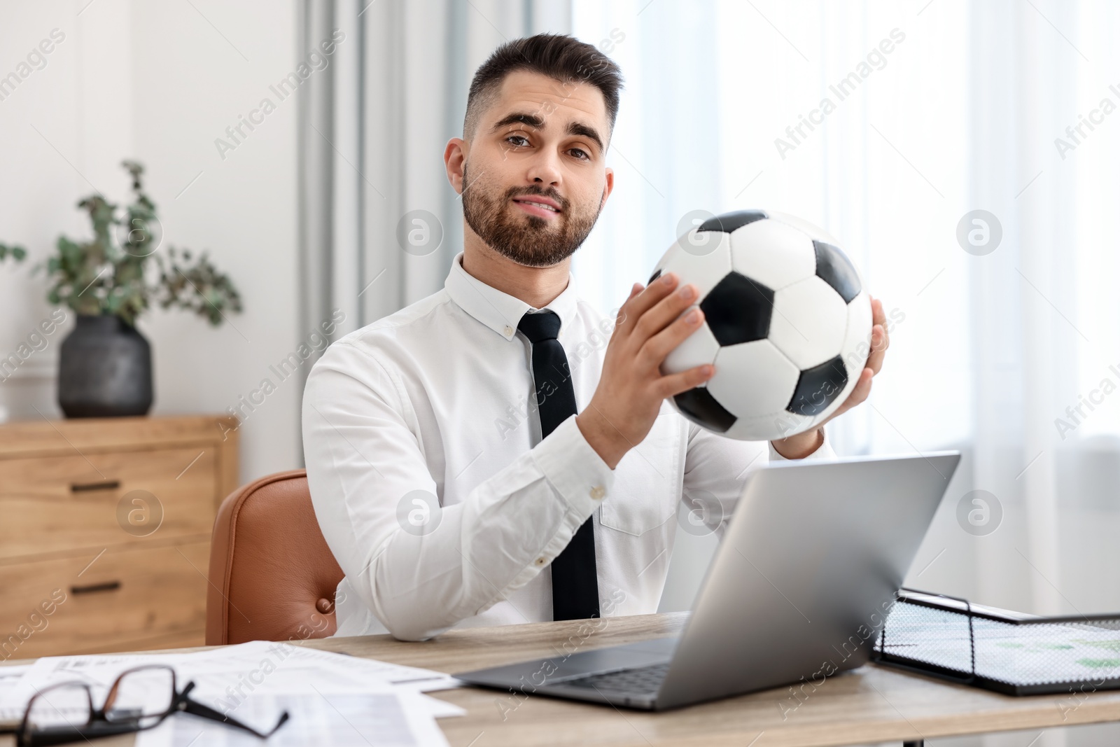 Photo of Young man with soccer ball at table in office