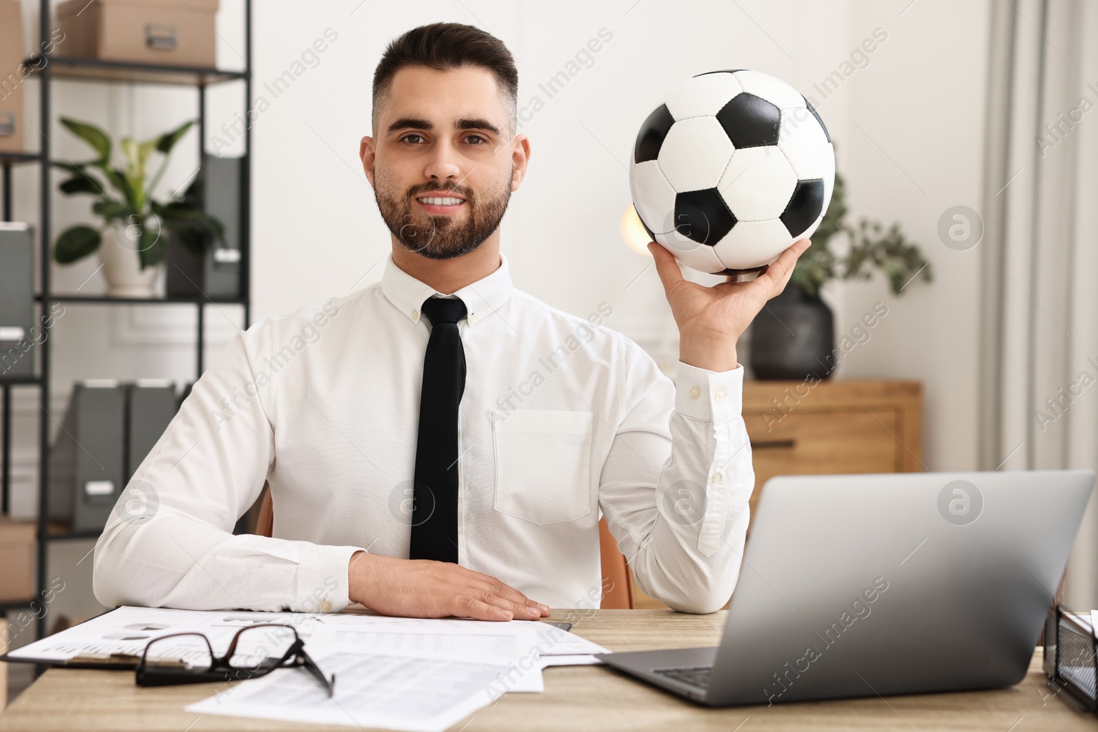 Photo of Young man with soccer ball at table in office