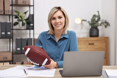 Smiling woman with american football ball at table in office