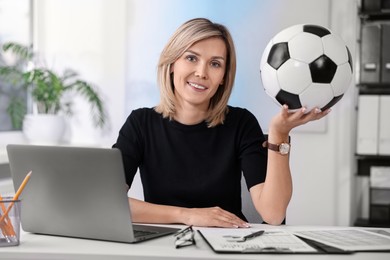 Photo of Smiling woman with soccer ball at table in office