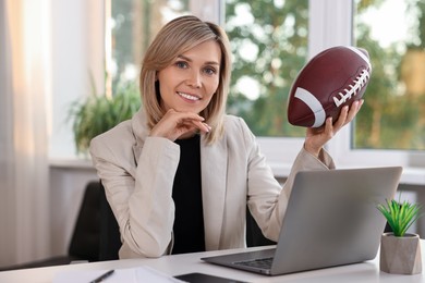 Photo of Smiling woman with american football ball at table in office