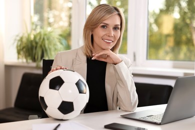 Smiling woman with soccer ball at table in office