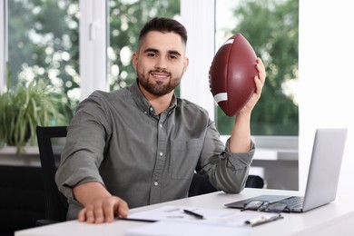 Photo of Young man with american football ball at table in office
