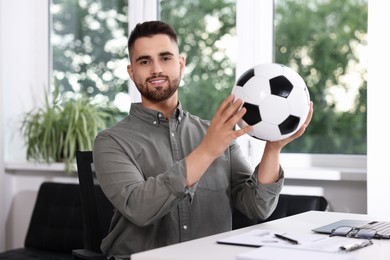 Photo of Young man with soccer ball at table in office