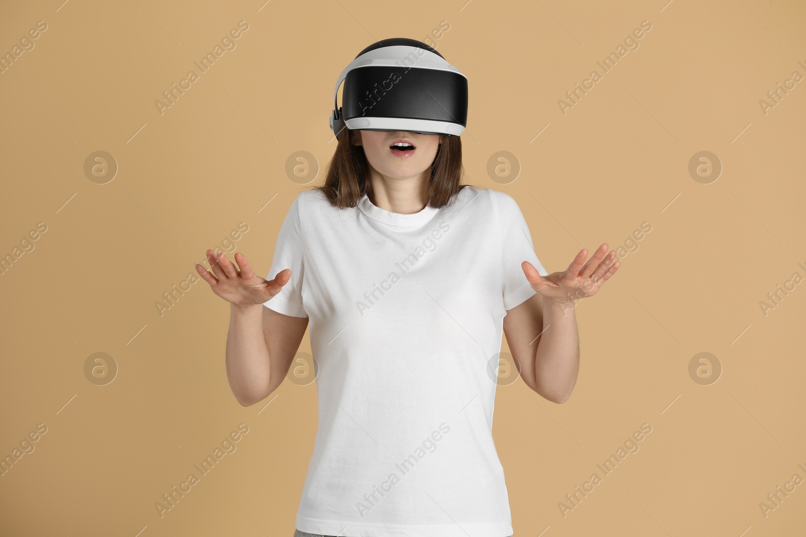 Photo of Surprised woman using virtual reality headset on beige background