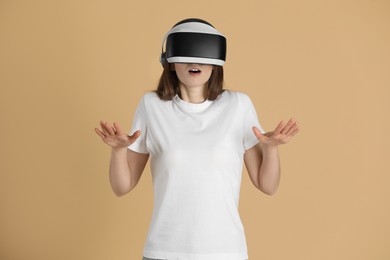 Surprised woman using virtual reality headset on beige background