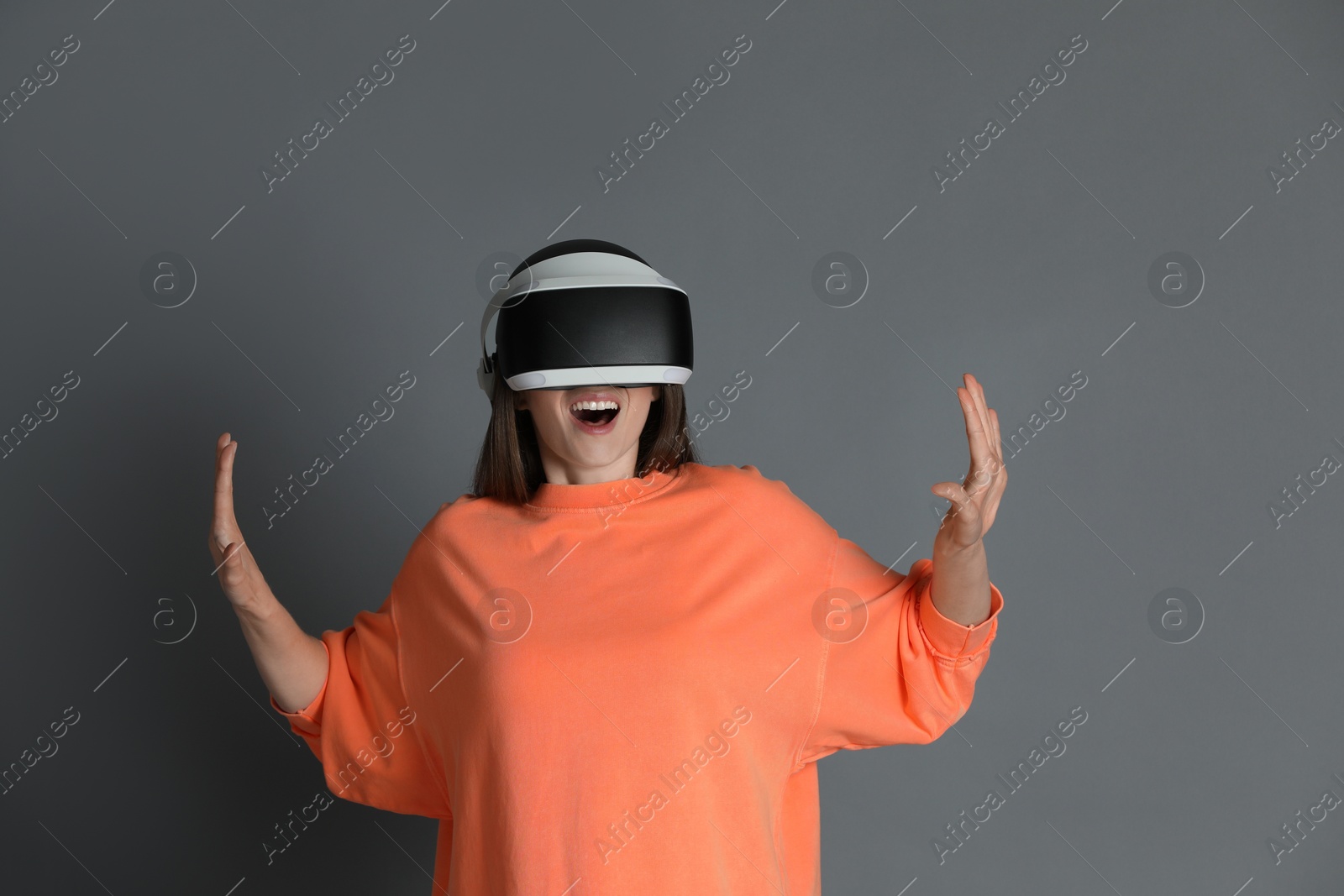 Photo of Surprised woman using virtual reality headset on gray background