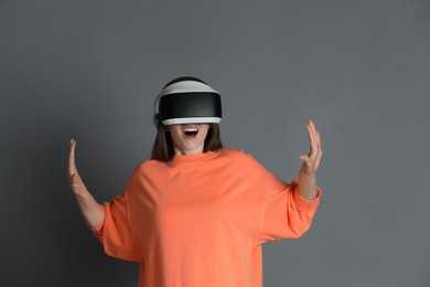 Surprised woman using virtual reality headset on gray background
