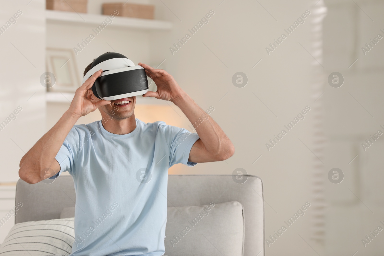 Photo of Smiling man using virtual reality headset at home, space for text