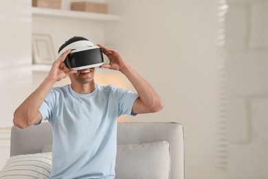 Photo of Smiling man using virtual reality headset at home, space for text