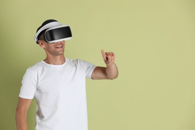 Photo of Smiling man using virtual reality headset on light green background, space for text